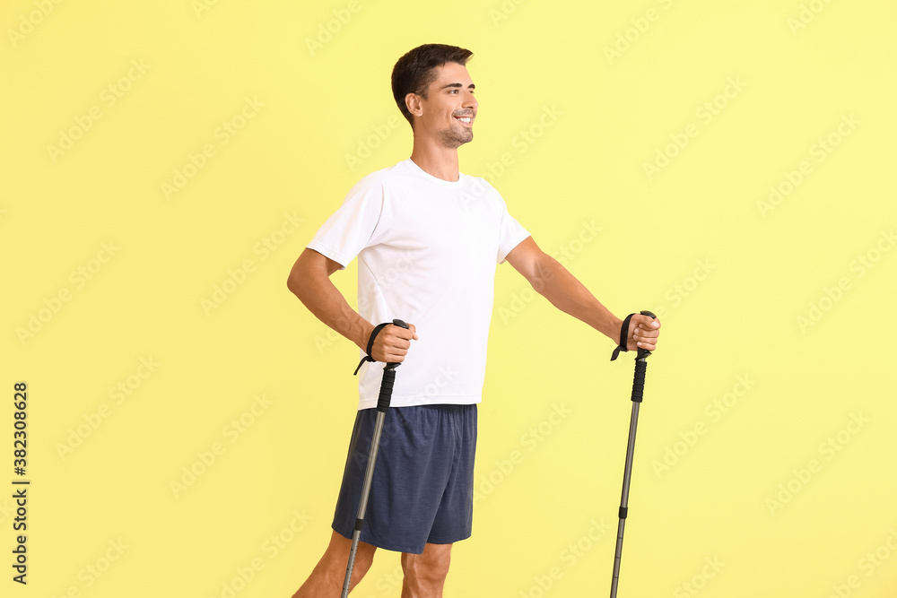 Young man with walking poles on color background
