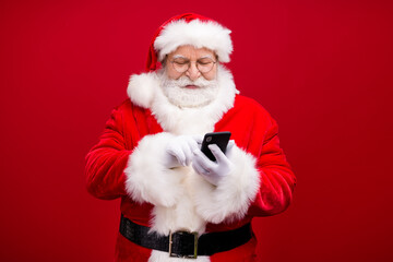 Wall Mural - Portrait of his he nice attractive handsome cheerful focused Santa father using device gadget 5g web service blog post smm comment isolated over bright vivid shine vibrant red color background