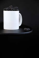 Blackberries portion inside a white mug on black background with copy space