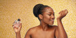 beauty, luxury and perfumery concept - portrait of happy smiling young african american woman with bare shoulders smelling perfume over golden glitter on background