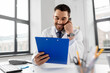 © Syda Productions - healthcare, medicine and people concept - smiling male doctor with clipboard calling on desk phone at hospital