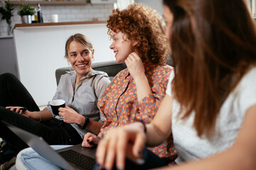 Wall Mural - Girlfriends talking and laughing in office. Beautiful women drinking coffee in the office.