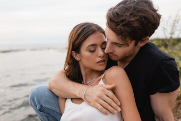 young man embracing brunette girlfriend on seaside
