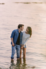 Wall Mural - Brunette woman touching boyfriend while standing in sea water at sunset