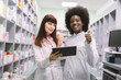 © sofiko14 - Two confident multiethnical female pharmacists in modern pharmacy. African American and Caucasian women chemists, making notes on tablet and showing thumbs up during inventory in pharmacy