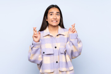 Wall Mural - Young Indian woman isolated on blue background with fingers crossing and wishing the best