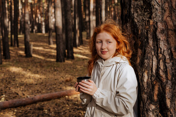 Red-haired girl drinking tea in the woods