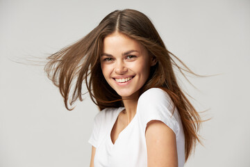 A woman with a beautiful smile looks ahead on a light background in a white T-shirt