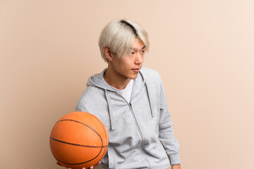 Wall Mural - Young asian man over isolated background with ball of basketball