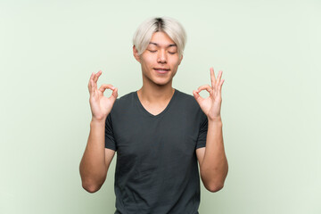 Wall Mural - Young asian man over isolated green background in zen pose