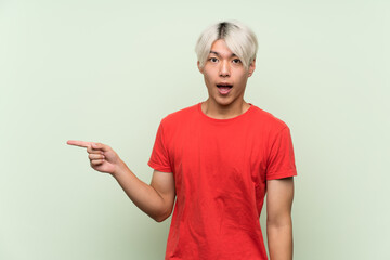 Wall Mural - Young asian man over isolated green background surprised and pointing finger to the side