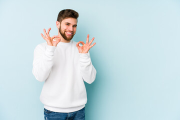 Canvas Print - Young caucasian man isolated on blue background cheerful and confident showing ok gesture.
