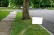 A white blank advertisement sign on a grassy strip near a street and a tree trunk