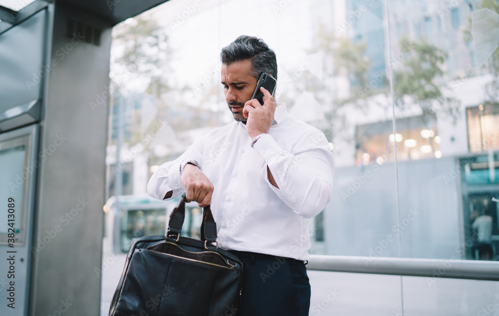 Middle aged male employee checking wrist watch time while waiting bus ...