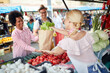 © luckybusiness - Seller woman selling fresh and organic vegetables at the green market or farmers market stall.  Young buyers choose and buy products for healthy food in grocery.
