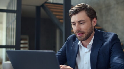 Smiling businessman working with laptop computer and papers in office.