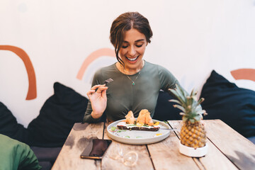 Cheerful young woman enjoying bruschetta with salmon while sitting in cozy restaurant