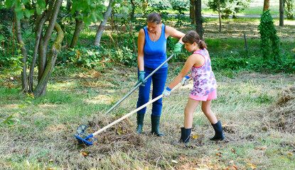 woman and her daughter work in the garden gathering the freshly cut dry grass