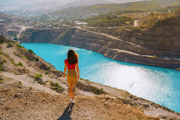 A beautiful woman in red clothes stands over a quarry with an azure lake, Kadykovsky quarry is a tourist natural attraction