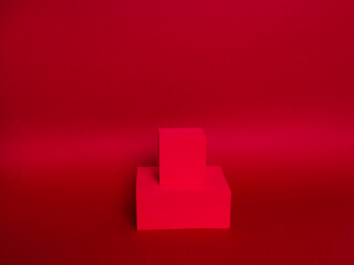 Photo of a bright podium (pedestal) of two cubes on a paper background. In dark red, with gradient. Advertising place. Blank product stand and abstract background with light.