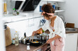 © LIGHTFIELD STUDIOS - young curly woman holding kitchen tongs while cooking eggs on frying pan in kitchen