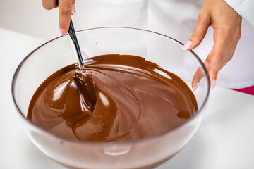 Closeup stirring mixing milk melted chocolate in glass bowl isolated on white background. Chocolatier make premium couverture hand-crafted chocolate. Candy making, pastry production, dessert concept