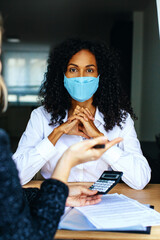 Wall Mural - Portrait of a business woman sitting at desk with mask and financial advisor holding calculator