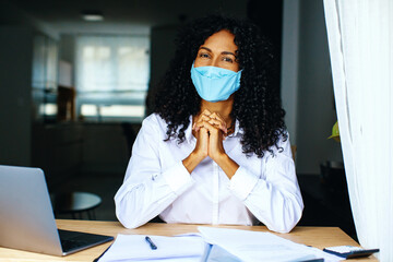 Wall Mural - Portrait of a happy business woman sitting at desk wearing face mask smiling at camera