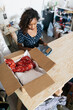 © Jesse Morrow/Stocksy - Young female business owner fashion entrepreneur packing clothing in box subscription delivery service