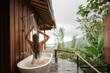Back view woman pampering her body in water while lie in bath tube outdoor with jungle and mountains view, take a shower