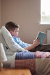 © Gourmet Photography/Stocksy - Boy reading a book while lying on a bed