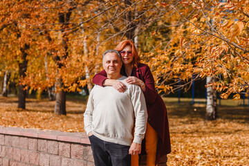 Happy husband and wife fall against the backdrop of beautiful yellow leaves. Woman hugs man