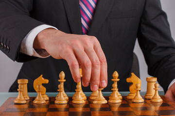 Wall Mural - Hand of businessman playing chess game. Close up male hand playing chess on wooden chessboard.