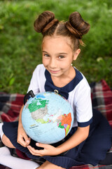 smiling school girl sitting on the grass with globe and magnifying glass