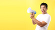 handsome Asian man over isolated yellow background shouting through a megaphone in studio With copy space.