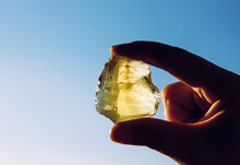 Person Hand Holding One Yellow Green Lemon Quartz Crystal Stone Against Sun And Blue Sky. Shiny, Copy Space.