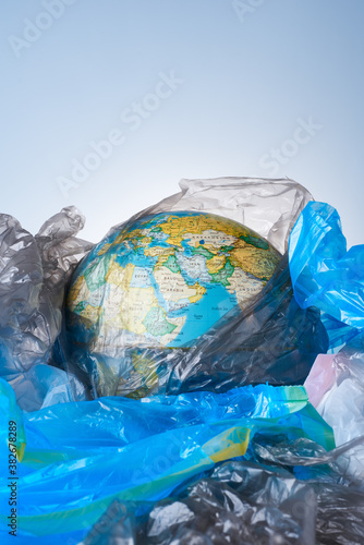 The concept of protecting the world from plastic waste, fighting environmental pollution, the globe lies in a pile of various garbage layouts on a light background.