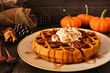 Pumpkin spice waffle with whipped topping, caramel and pecans. Side view table scene with a dark wood background. Fall breakfast concept.