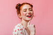© Look! - Beautiful woman with red hair covers her face with her hands. Girl in t-shirt with cherries cute smiles on pink background