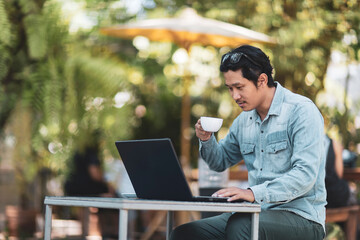 Young asian man using laptop at home while sitting the wooden table.Male hands typing on the notebook keyboard.Man using laptop for online working at home.