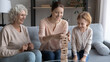 © fizkes - Happy family playing funny board game, enjoying leisure time, sitting on cozy couch at home, smiling young woman with little daughter and mature mother having fun, building tower from wooden blocks