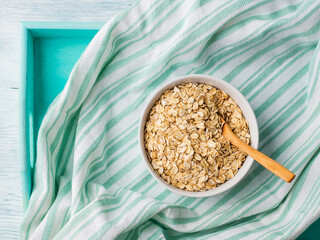 Gluten free oatmeal flakes in white bowl on green turquoise napkin background. Top view