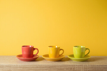 Coffee cups on wooden shelf over yellow wall background