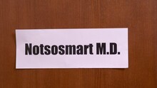 Wooden Door Opens To The Office Of Quack Doctor, On Which Hangs Sign With Funny Name, Close Up, Blurred Background. Perception Of Serious Social Problems Through Humor.