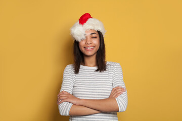 Wall Mural - Happy black woman in Santa hat making a wish on yellow background