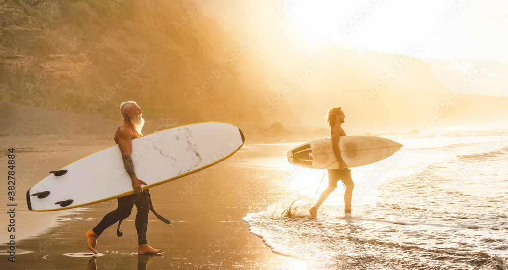 Happy friends with different age surfing together on tropical ocean - Sporty people having fun during vacation surf day - Elderly and youth people sport lifestyle concept - obrazy, fototapety, plakaty 