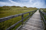 Fototapeta Pomosty - wooden jetty for direction beach through the dunes on a cloudy sky