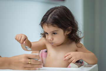 two year old girl eats yogurt with a spoon, middle plane