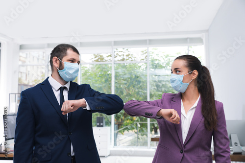 Office employees in masks greeting each other by bumping elbows at workplace