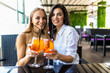 © F8  \ Suport Ukraine - Young women drinking aperol spritz, clink glasses with friends, looking at camera in modern cafe